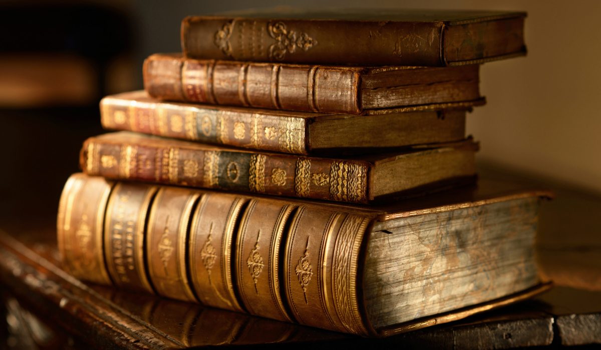 Vintage,,Antiquarian,Books,Pile,On,Wooden,Surface,In,Warm,Directional