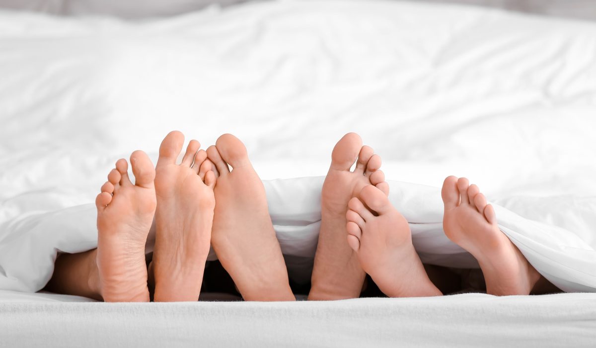 Feet,Of,Man,And,Two,Women,Lying,Under,Blanket,In